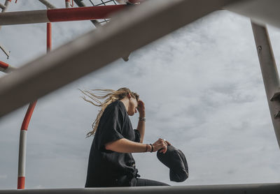 Woman sitting on built structure against sky