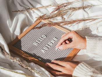 Woman in white knitted sweater typing hello autumn on letter board. season greeting concept. 