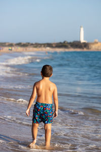 Funny kid enjoying the water of the ocean with a lighthouse background