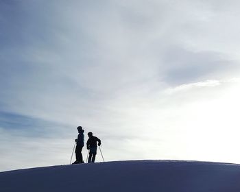 Silhouette friends skiing on snow against sky during sunny day