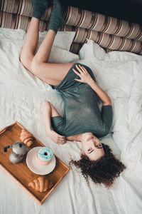 High angle view of woman day dreaming while lying by food on bed