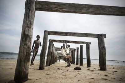 Men standing on wooden posts at beach against sky