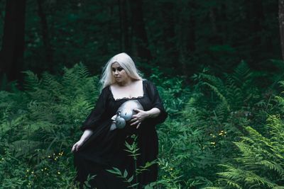 Woman holding mask while standing amidst plants