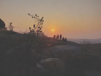 Silhouette people on land against sky during sunset