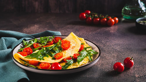 French omelette filled with cherry tomatoes and arugula on a plate on the table web banner