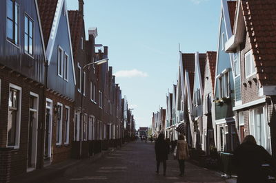 People walking on narrow street in city against sky