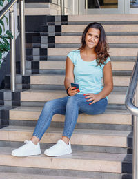 Young women with mobile phone sits on the steps and smiling