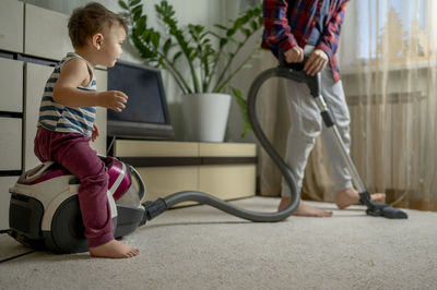 Boy cleaning carpet with brother sitting on vacuum cleaner at home