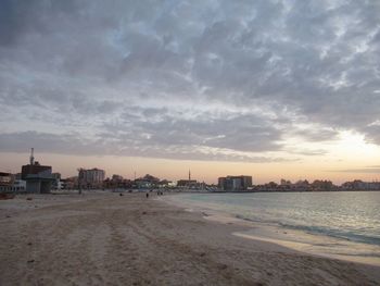 Scenic view of beach by buildings against sky during sunset