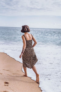 Rear view of woman walking on beach against sea