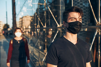 Young man walking in the city center along glass store front in the evening, looking away