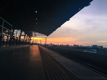 Railroad tracks by silhouette bridge against sky during sunset