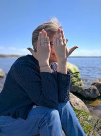 Midsection of woman sitting by sea against blue sky