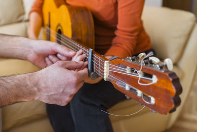 Cropped hands of man assisting woman in playing guitar at home