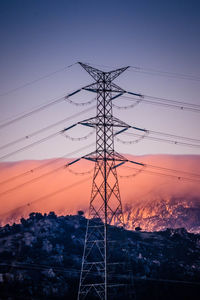 Low angle view of electricity pylon against sky during sunset