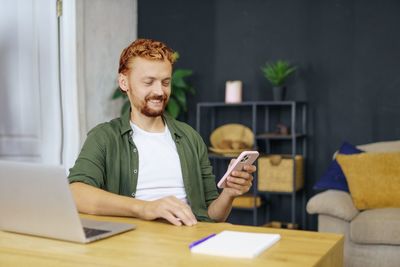 Portrait of young man using mobile phone while sitting at home