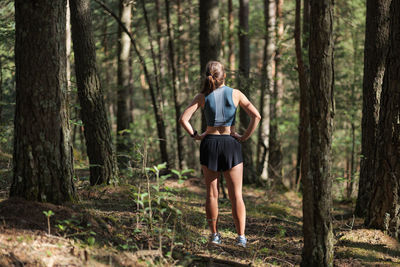 Rear view of female trail runner dressed in sportswear standing on trail in the forest