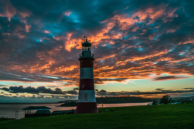 Lighthouse by building against sky during sunset