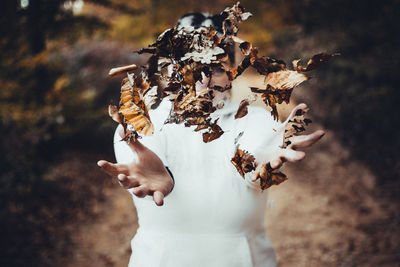 Woman throwing dried autumn leaves in forest