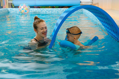 Toddler child learning to swim in indoor swimming pool with teacher. floating in the water