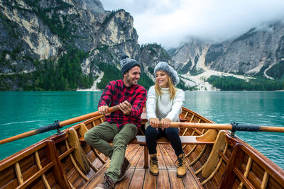 Rear view of people sitting on lake against mountains