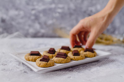 Cropped hand of person picking cookie from tray on table