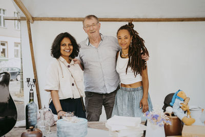 Portrait of smiling male and female partners standing together in stall at flea market