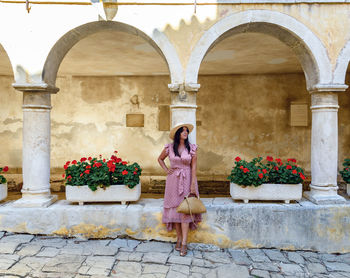Young woman in pink summer dress standing in old town square.