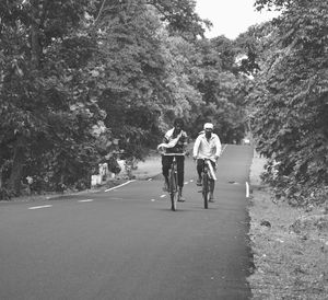 Rear view of friends walking on road amidst trees