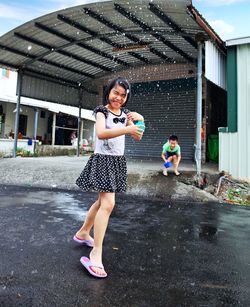 Full length of boy and girl playing with water on footpath