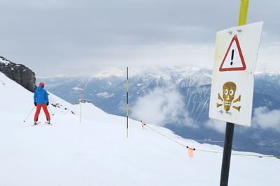 Rear view of person standing next to danger sign board against cloudy sky