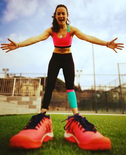 Low angle view of woman with arms outstretched wearing large shoes on field