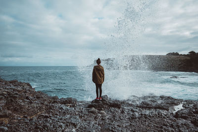 Rear view of man standing on sea shore against sky