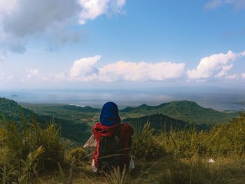 Rear view of woman sitting on mountain against sky