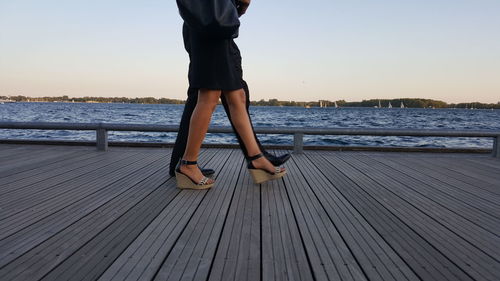 Side view of couple walking on pier over sea against clear sky