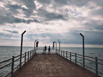 People on pier over sea against sky