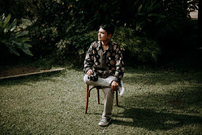 Full length of young woman looking away while sitting on tree