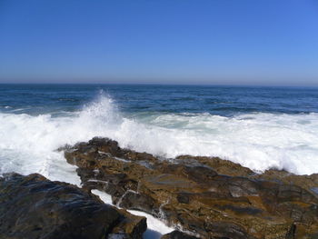 Waves splashing on sea against clear blue sky