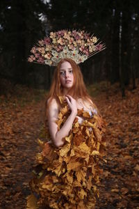 Thoughtful young woman wearing flowers on hair standing at forest during autumn