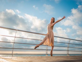 Mid adult woman standing by railing against cloudy sky during sunset