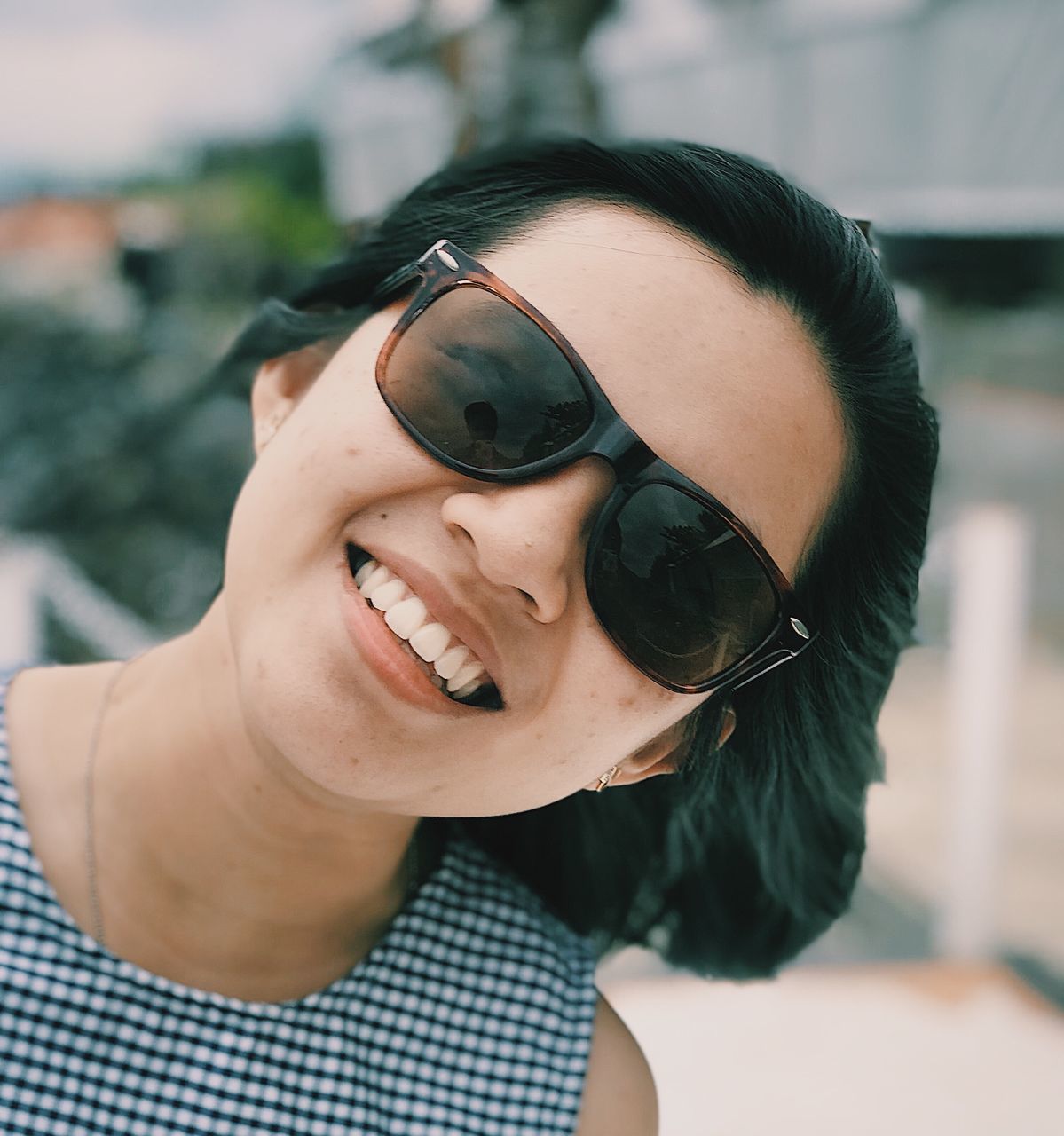 CLOSE-UP PORTRAIT OF SMILING YOUNG WOMAN WEARING SUNGLASSES