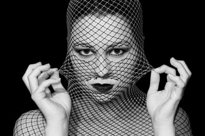 Close-up portrait of woman with hand against black background