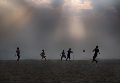 Silhouette people playing on beach against sky