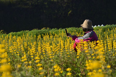 Side view of woman photographing with mobile phone while sitting amidst flowers