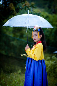 Portrait of young woman with umbrella standing against trees
