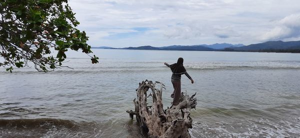 Rear view of man standing at beach against sky