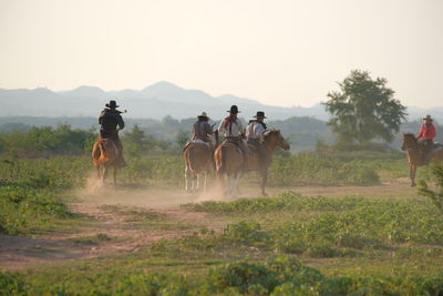 People riding horses on field against sky