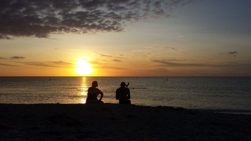 Silhouette men standing on beach against sky during sunset