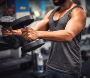 Midsection of young man lifting dumbbell in gym