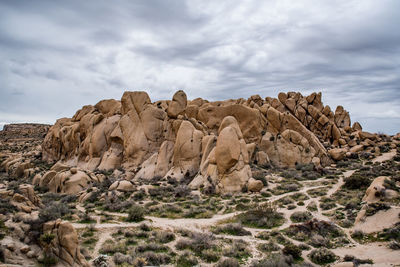 Massive boulder mound in center of desert landscape under cloudy sky